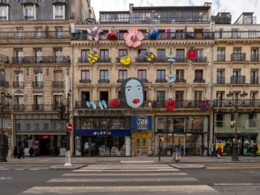 Façade d'immeuble parisien ornée de grandes décorations colorées, dont un visage et des coccinelles.