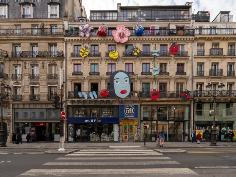 Façade d'immeuble parisien ornée de grandes décorations colorées, dont un visage et des coccinelles.