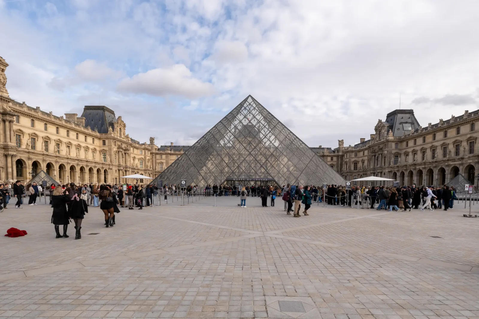 La Pyramide du Louvre en verre, entourée de bâtiments historiques et de nombreux visiteurs.