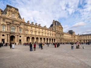 Le majestueux Palais du Louvre et sa cour pavée animée sous un ciel nuageux.