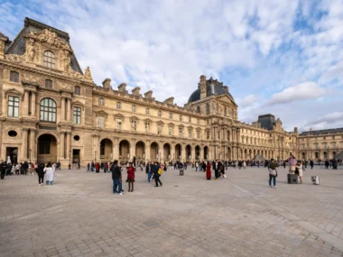 Le majestueux Palais du Louvre et sa cour pavée animée sous un ciel nuageux.