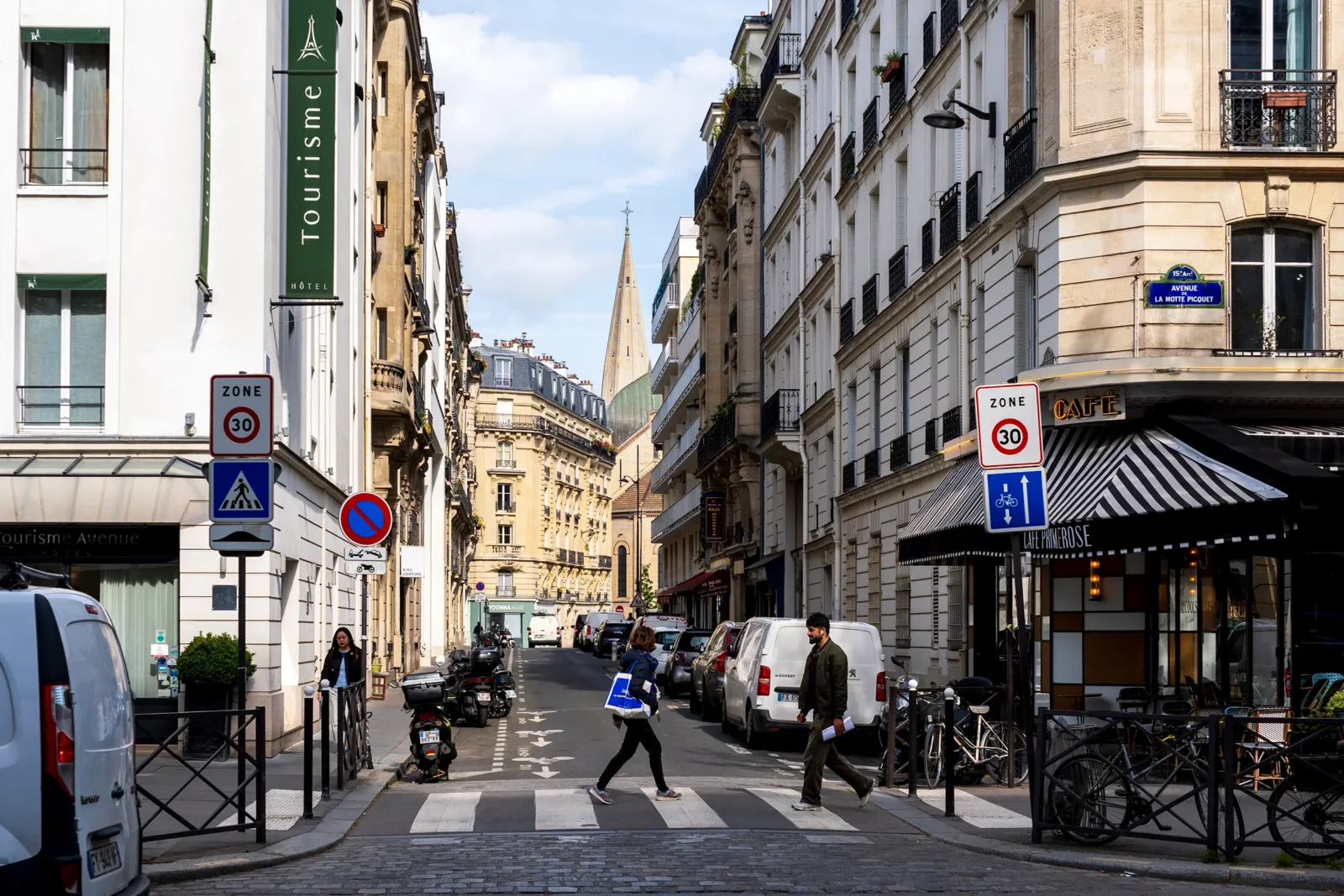 Une rue parisienne animée avec des piétons, des voitures et une église au loin.
