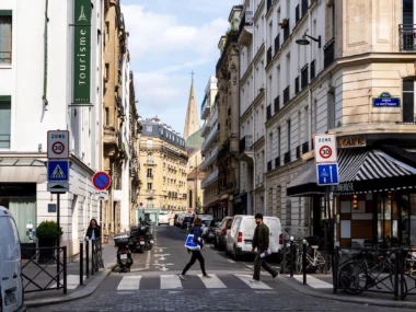 Une rue parisienne animée avec des piétons, des voitures et une église au loin.
