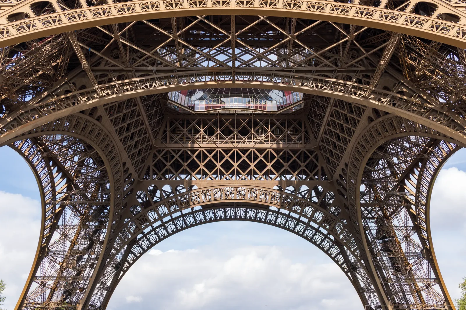 Vue d'en bas de la Tour Eiffel, révélant sa structure métallique complexe sous un ciel nuageux.