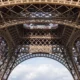 Vue d'en bas de la Tour Eiffel, révélant sa structure métallique complexe sous un ciel nuageux.