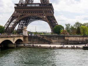 La Tour Eiffel surplombe la Seine où des gens se reposent sur les marches ensoleillées.