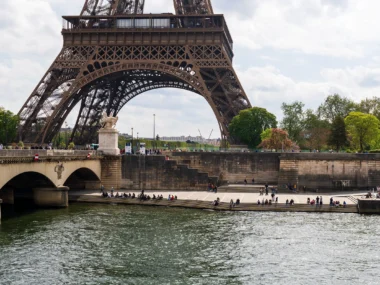 La Tour Eiffel surplombe la Seine où des gens se reposent sur les marches ensoleillées.