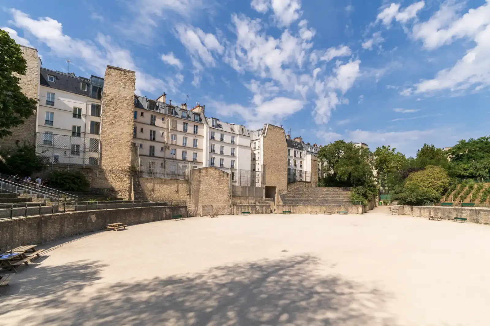 Vue ensoleillée des anciennes Arènes de Lutèce bordées par des immeubles parisiens.