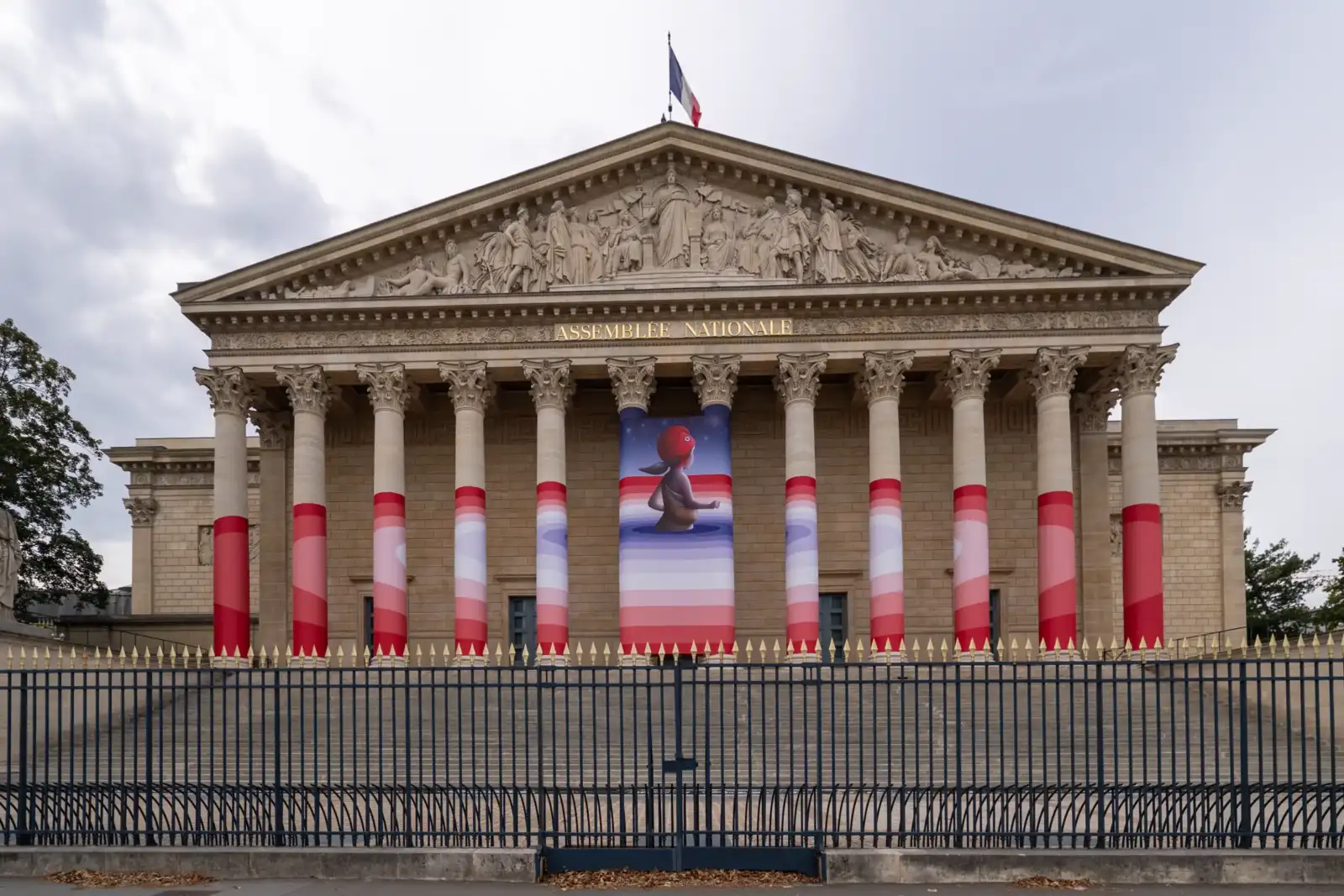 La façade de l'Assemblée nationale avec ses colonnes habillées d'une bannière artistique rose.