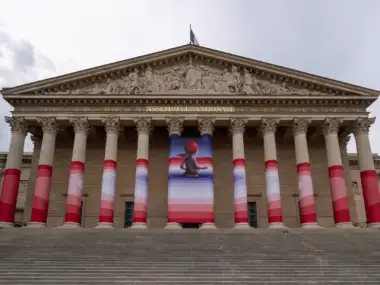 Façade de l'Assemblée Nationale à Paris décorée de bandes rouges pour une exposition artistique.