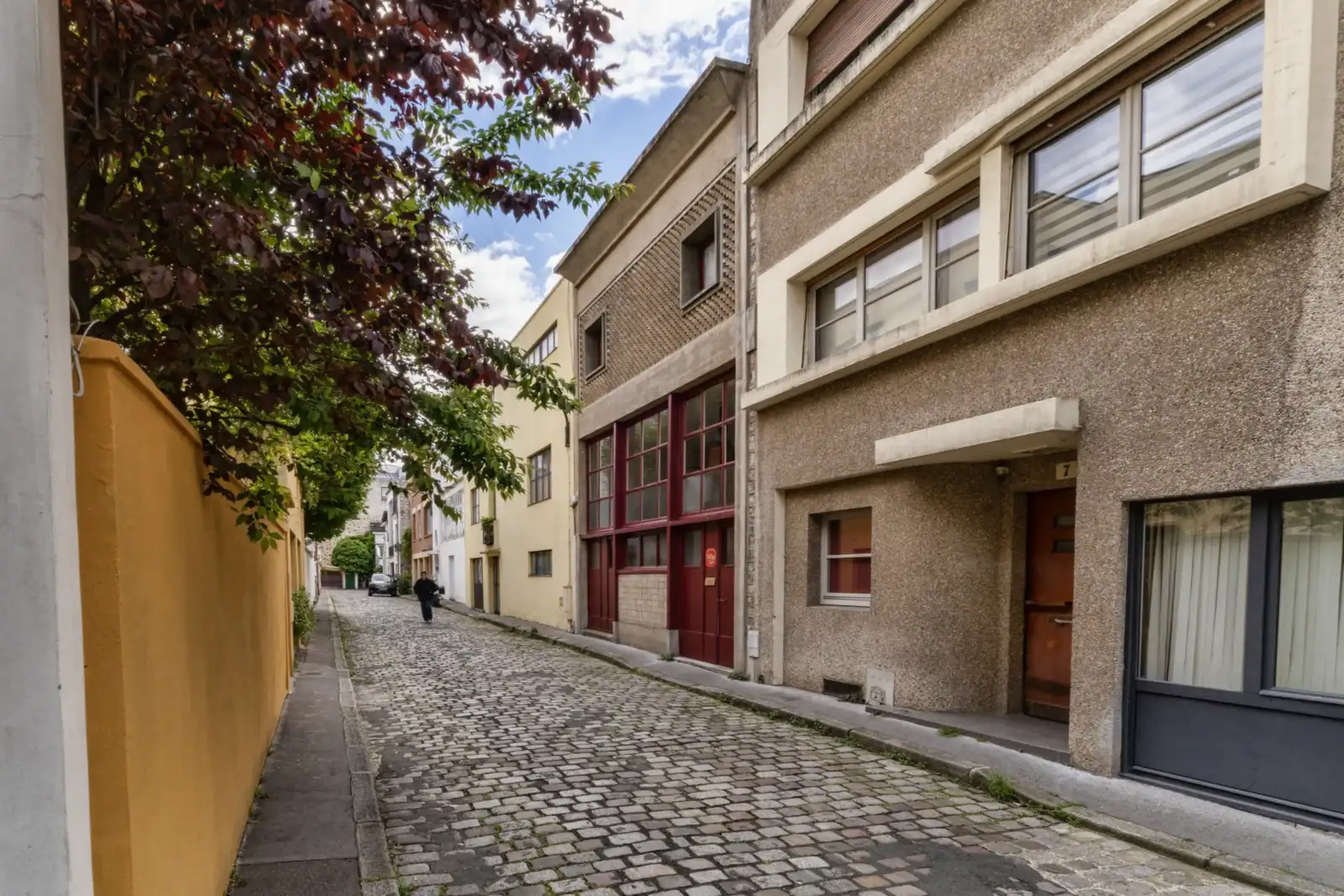 Une ruelle pavée de Paris bordée de bâtiments historiques et d'arbres feuillus.