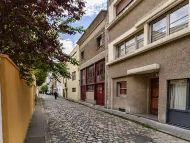 Une ruelle pavée de Paris bordée de bâtiments historiques et d'arbres feuillus.