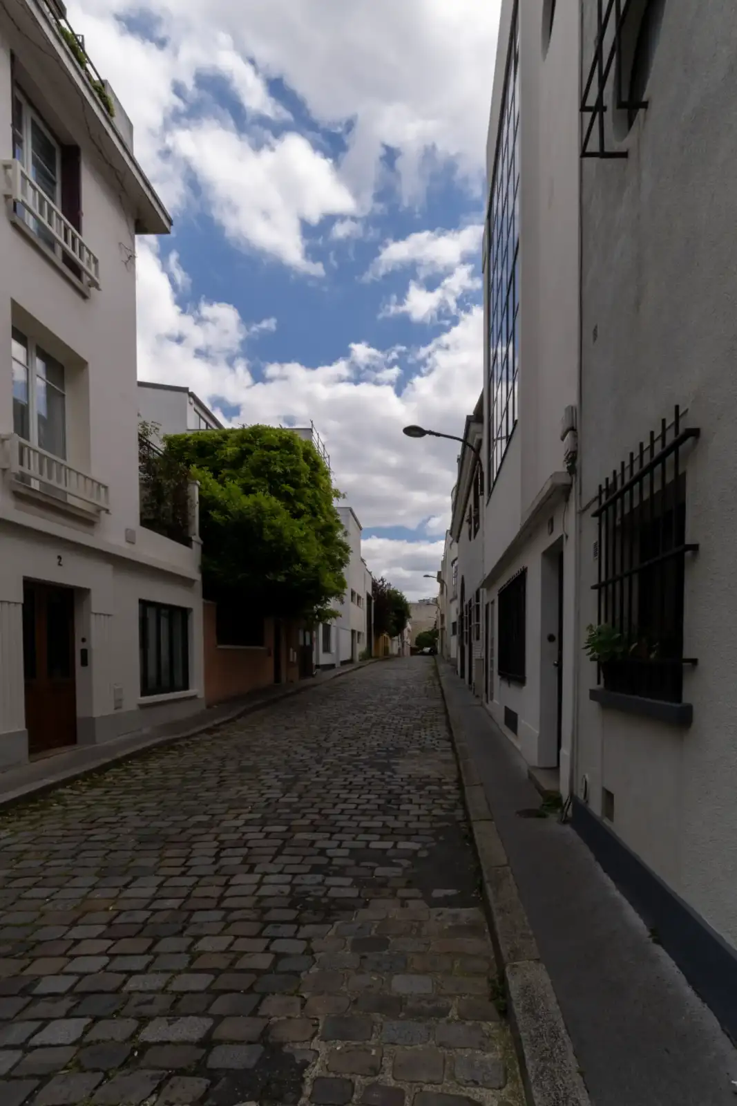 Une rue pavée bordée de bâtiments blancs sous un ciel nuageux à Paris.
