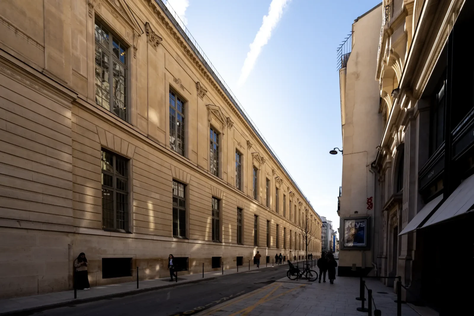 La façade classique de la Bibliothèque nationale de France domine une rue parisienne ensoleillée.