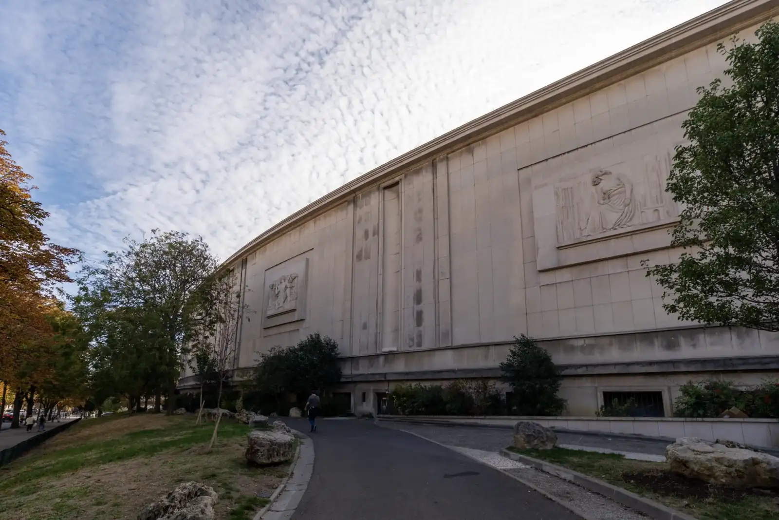 Vue extérieure d'un grand bâtiment en pierre avec des bas-reliefs sous un ciel nuageux.