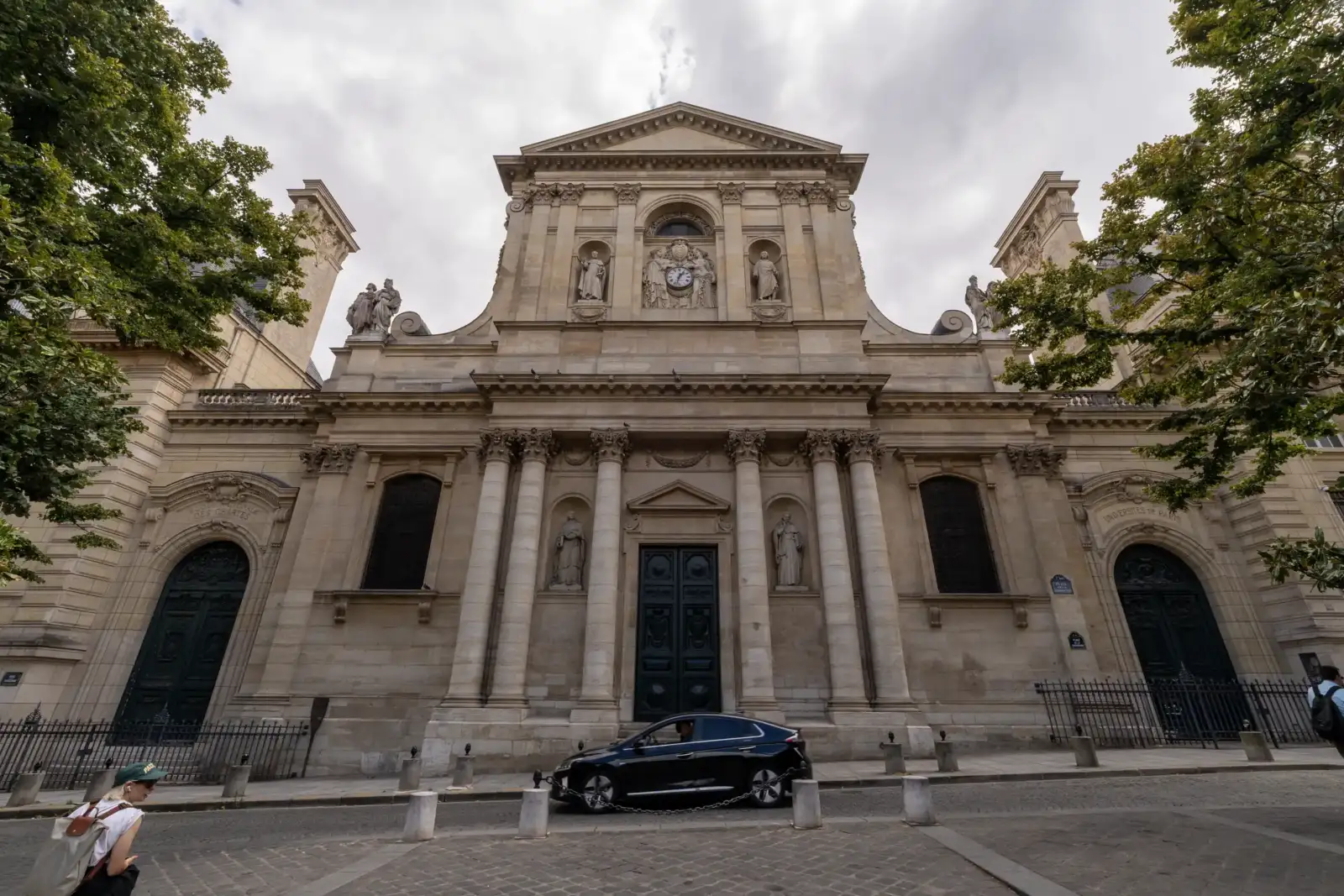 Vue en contre-plongée de la façade classique de la Sorbonne sous un ciel nuageux.