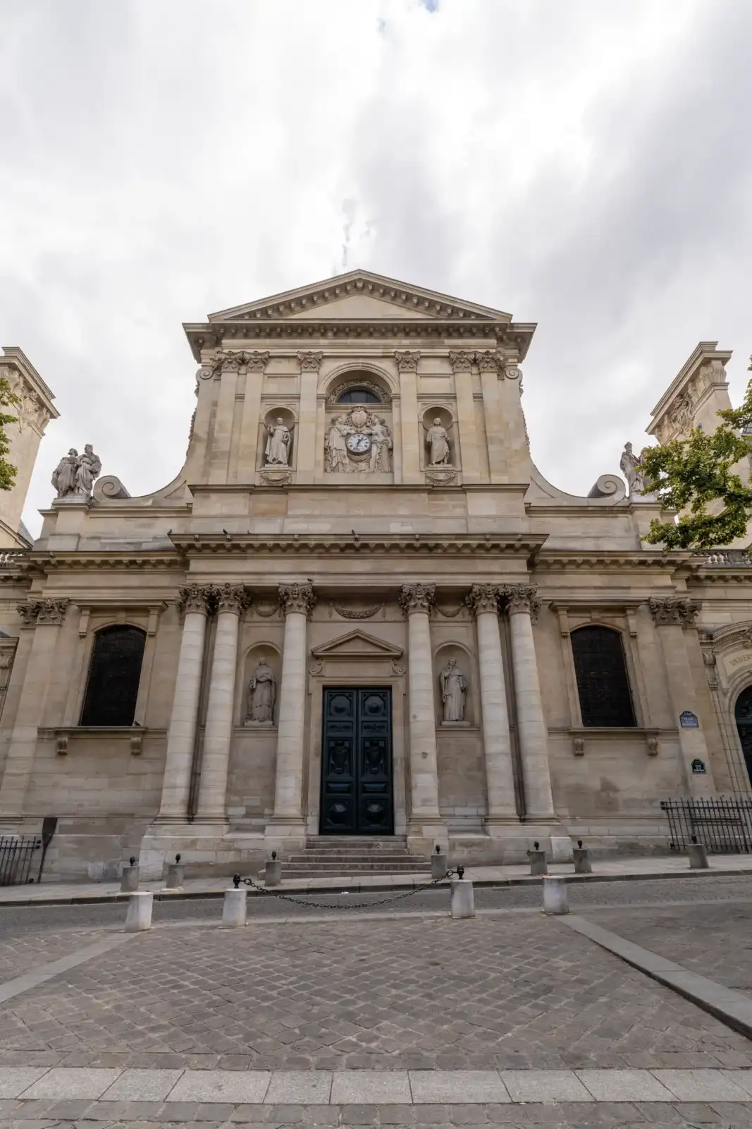 La façade classique en pierre de la bibliothèque interuniversitaire de la Sorbonne sous un ciel nuageux.