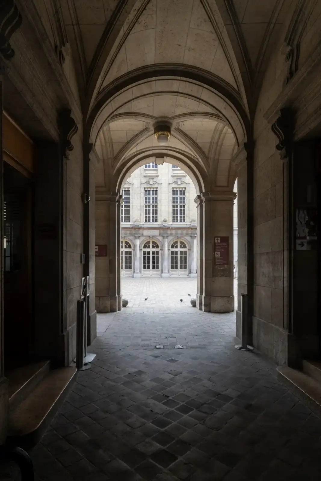 Vue ombragée depuis un couloir voûté en pierre vers une cour extérieure lumineuse.