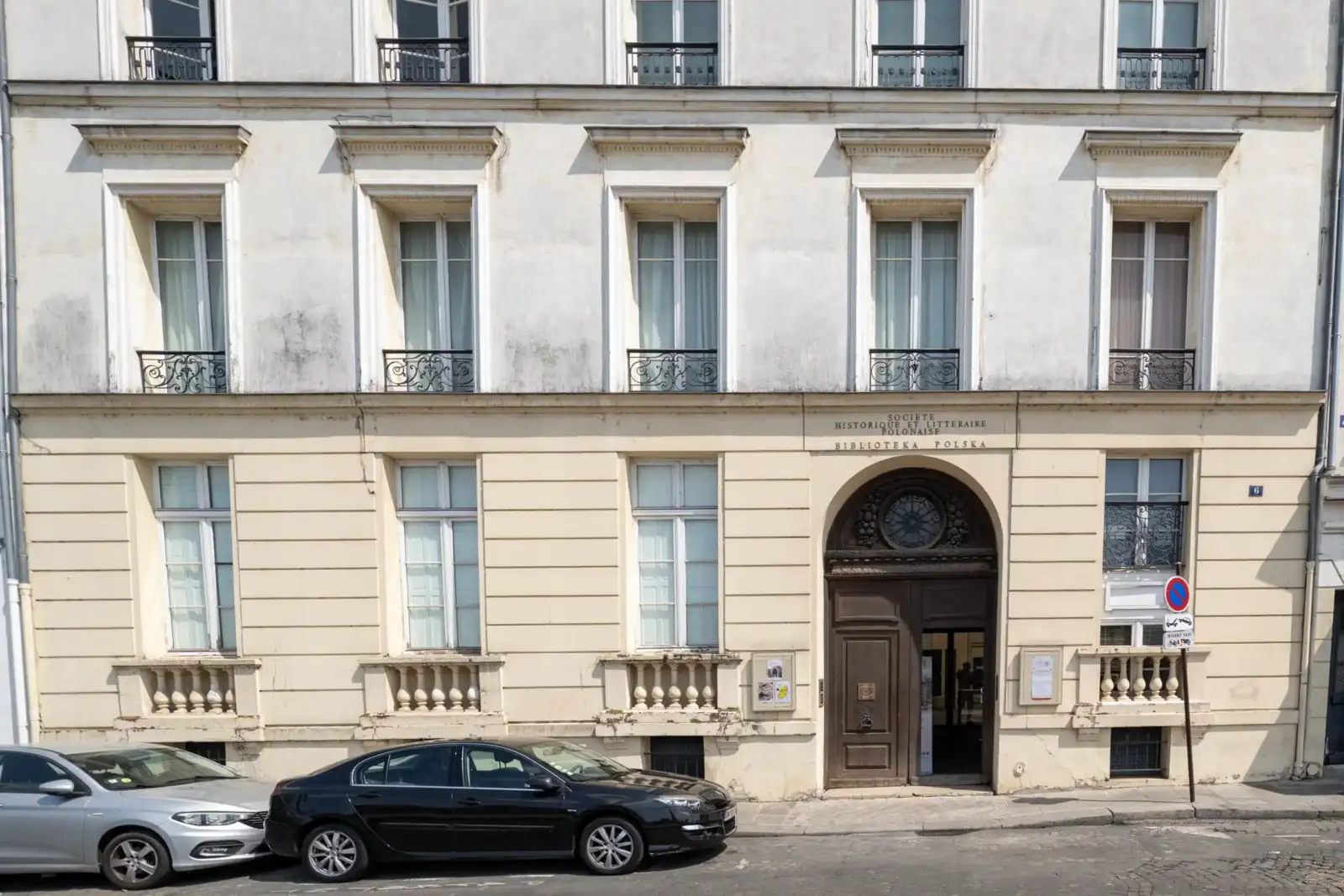 Façade claire de la Bibliothèque polonaise de Paris avec deux voitures garées en bas.