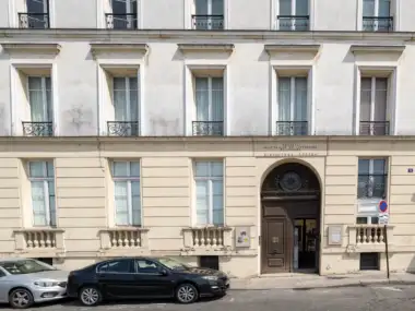 Façade claire de la Bibliothèque polonaise de Paris avec deux voitures garées en bas.