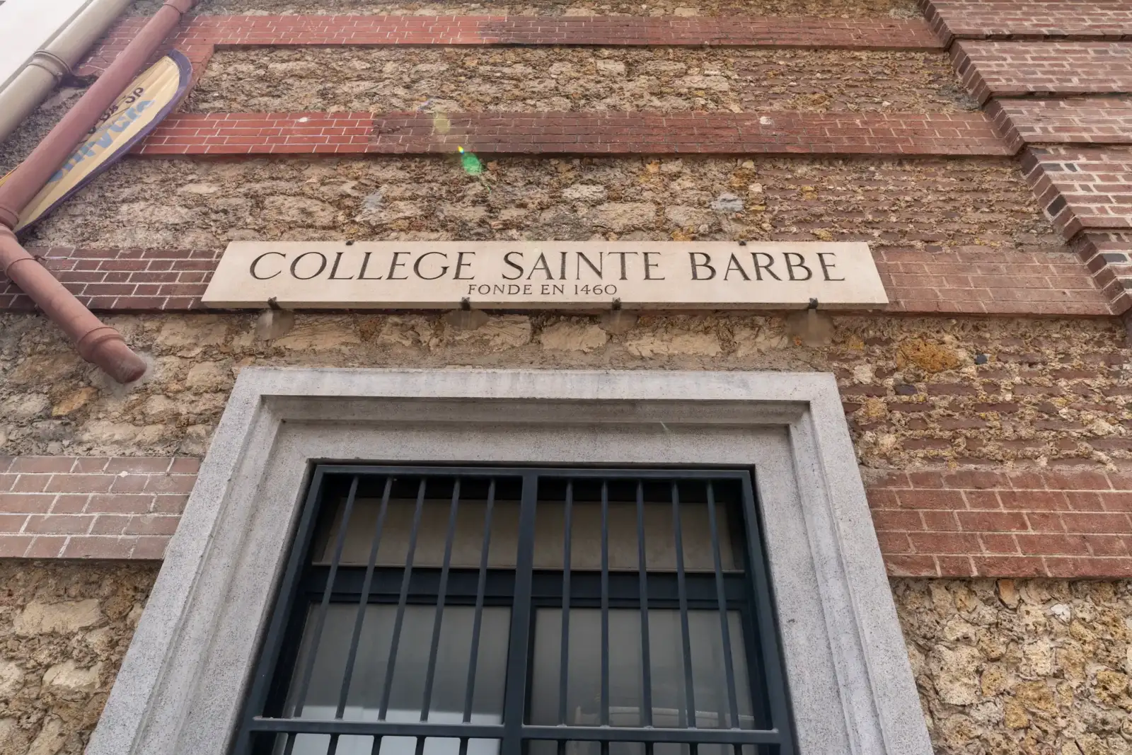 Une plaque en pierre indiquant College Sainte Barbe sur un mur ancien.