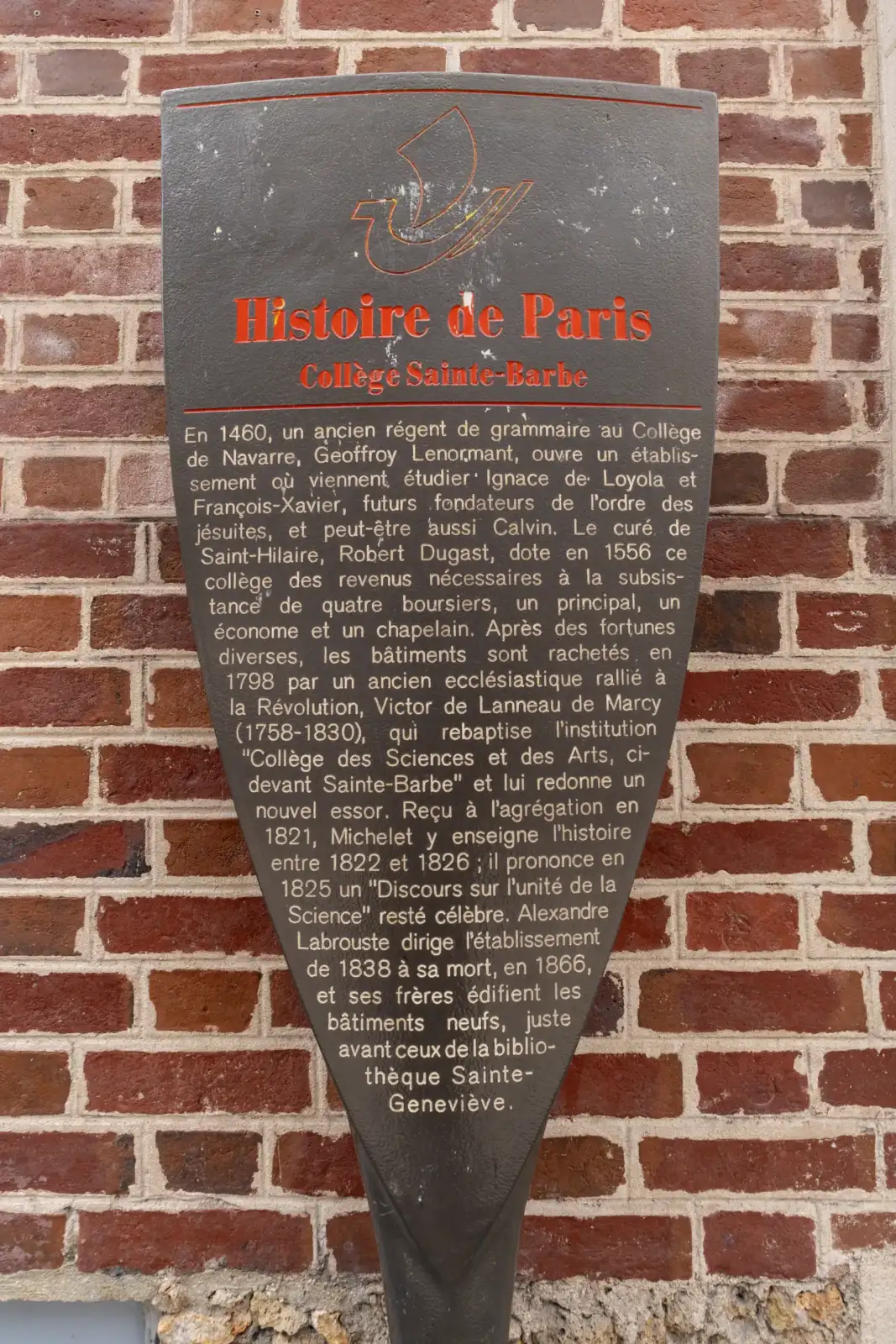 Une plaque historique murale rouge et noire fixée sur un mur de briques.