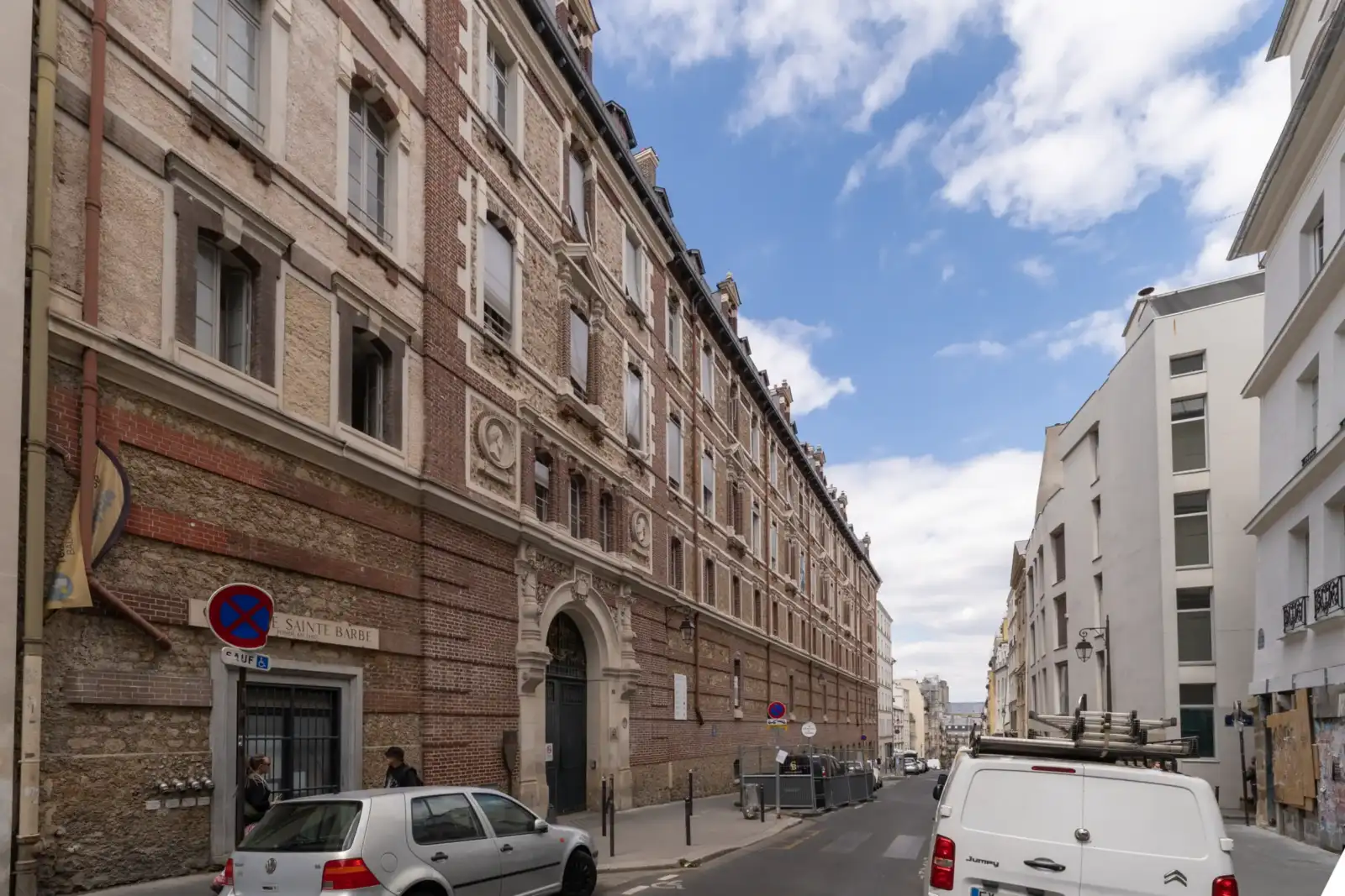 Vue de rue de la bibliothèque Sainte-Barbe à Paris avec des voitures garées.