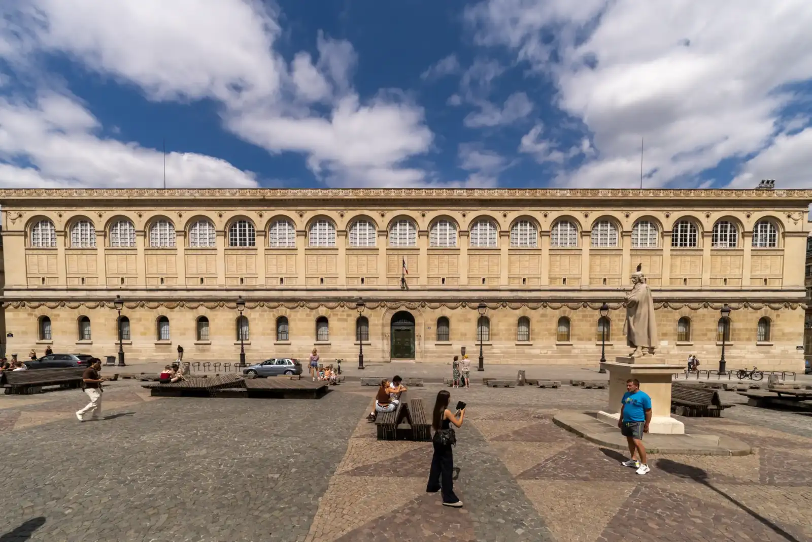 Vue large de la façade classique de la bibliothèque Sainte Geneviève sous un ciel nuageux.