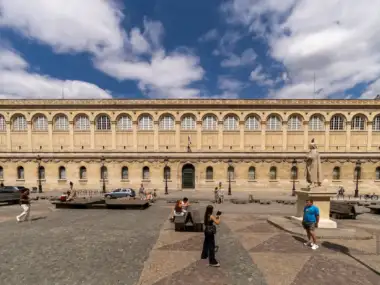 Vue large de la façade classique de la bibliothèque Sainte Geneviève sous un ciel nuageux.