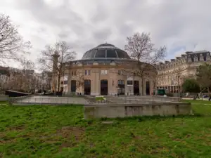La façade arrondie de la Bourse de commerce domine un jardin urbain sous ciel nuageux.