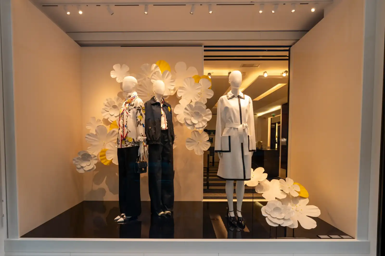 Trois mannequins présentent des vêtements élégants dans la vitrine fleurie d'une boutique Chanel parisienne.