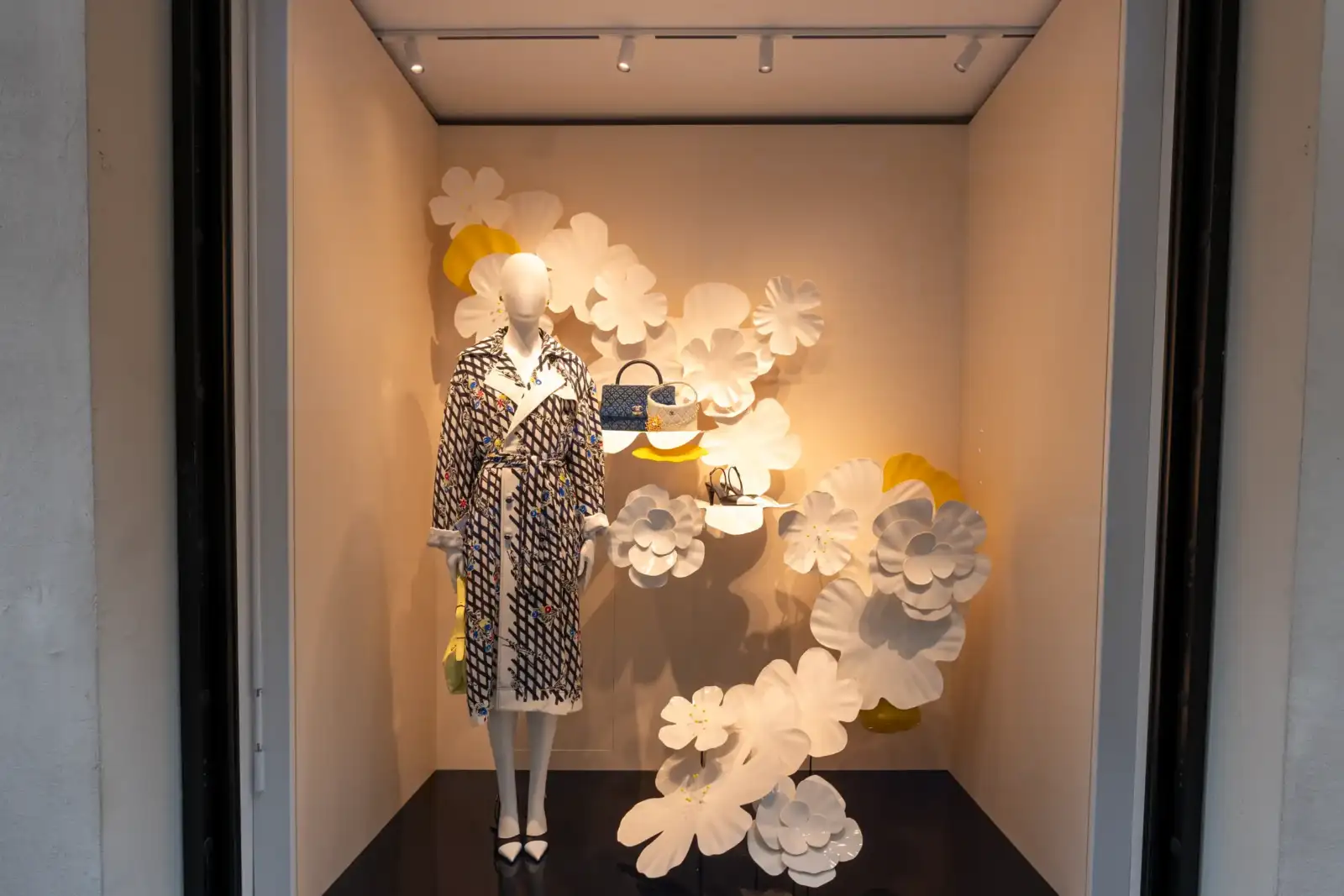 Un mannequin porte un manteau Chanel devant des fleurs décoratives dans une vitrine parisienne.