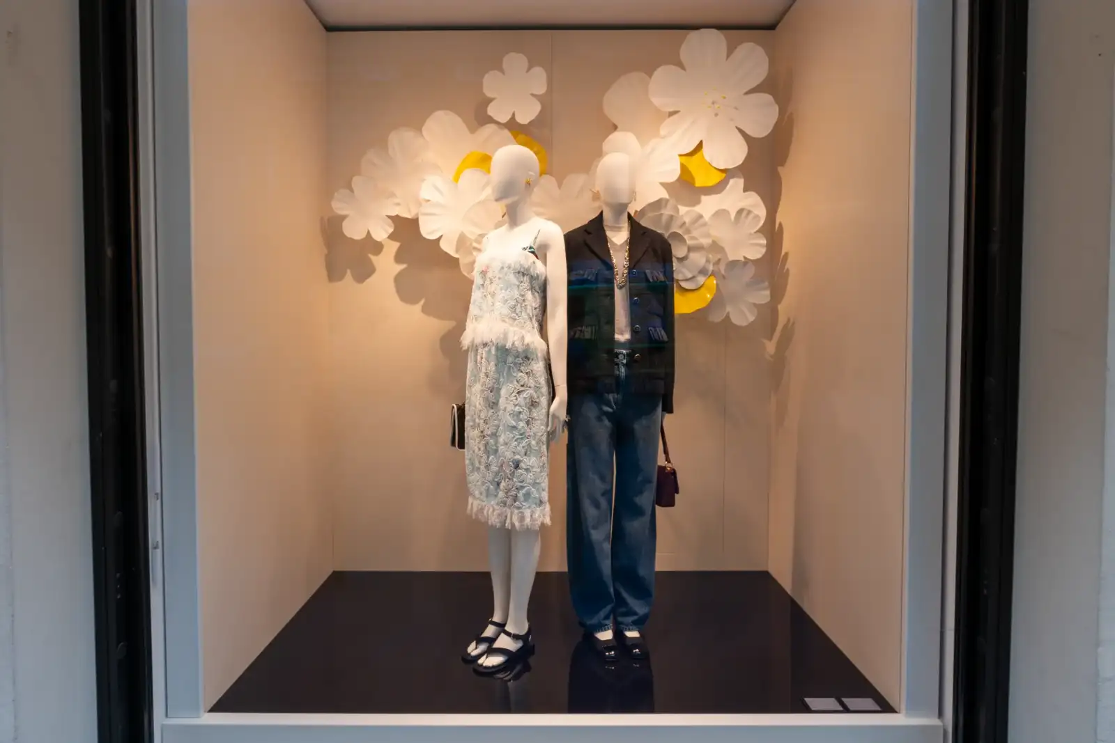 Deux mannequins Chanel habillés de vêtements élégants devant un décor floral en papier blanc.