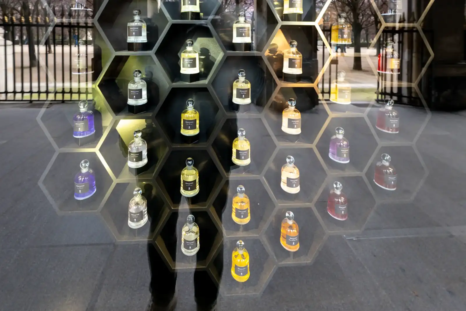 Des flacons de parfum Serge Lutens sont exposés dans des niches hexagonales rétroéclairées élégantes.