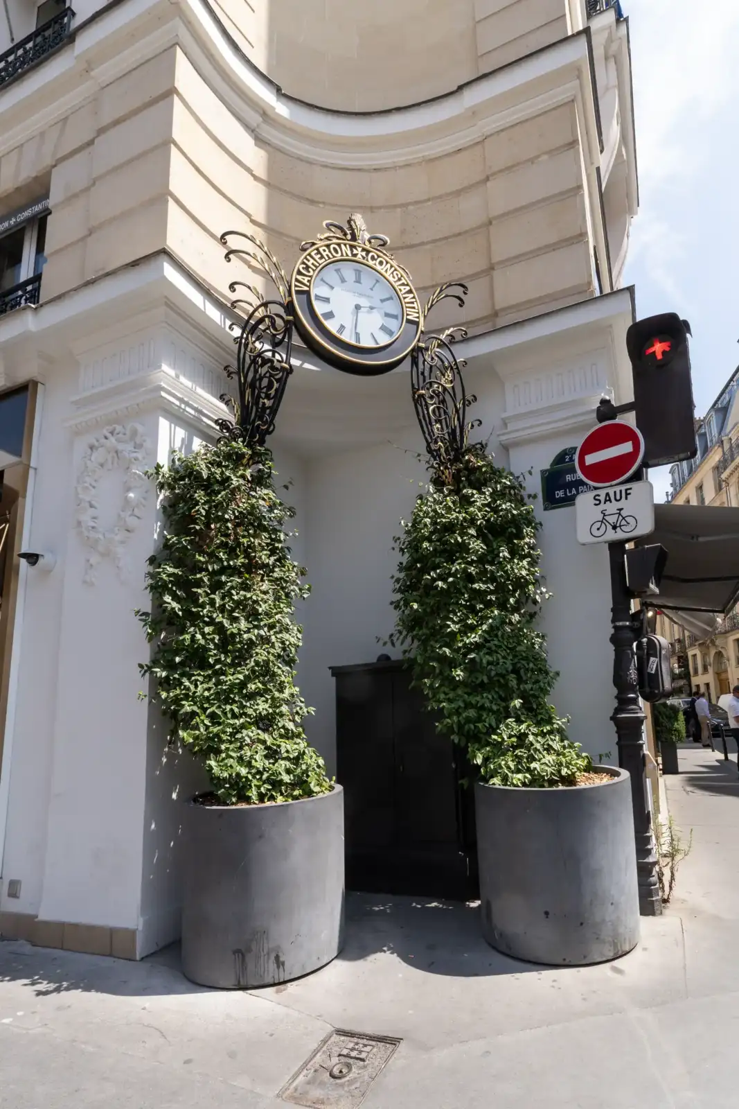 Façade de la boutique Vacheron Constantin à Paris avec deux grands bacs végétalisés et une grande horloge suspendue.