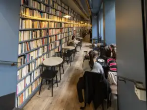 Des clients sont assis dans un café parisien bordé par d'immenses étagères de livres.
