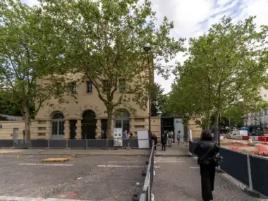 Vue extérieure de l'entrée des catacombes de Paris avec des visiteurs et des arbres.