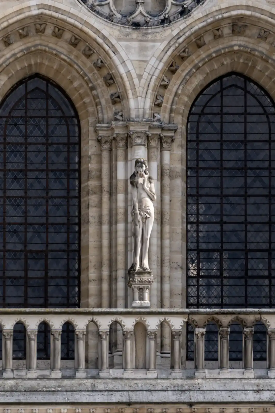 Une statue de femme se dresse entre deux hautes fenêtres gothiques de Notre-Dame.