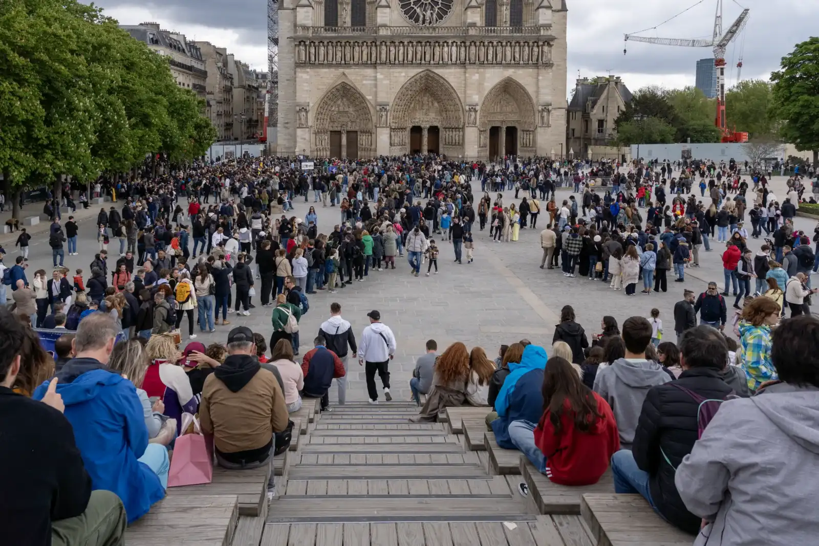 Une foule de touristes se rassemble devant la cathédrale Notre-Dame sous un ciel nuageux.