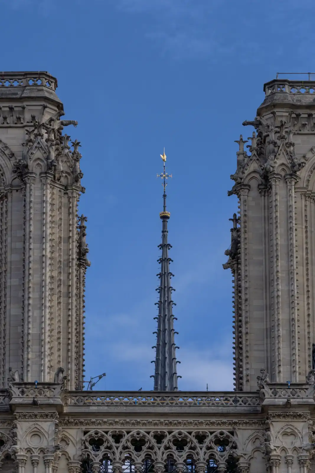 La flèche dorée de Notre-Dame de Paris s'élève entre deux tours gothiques sculptées.