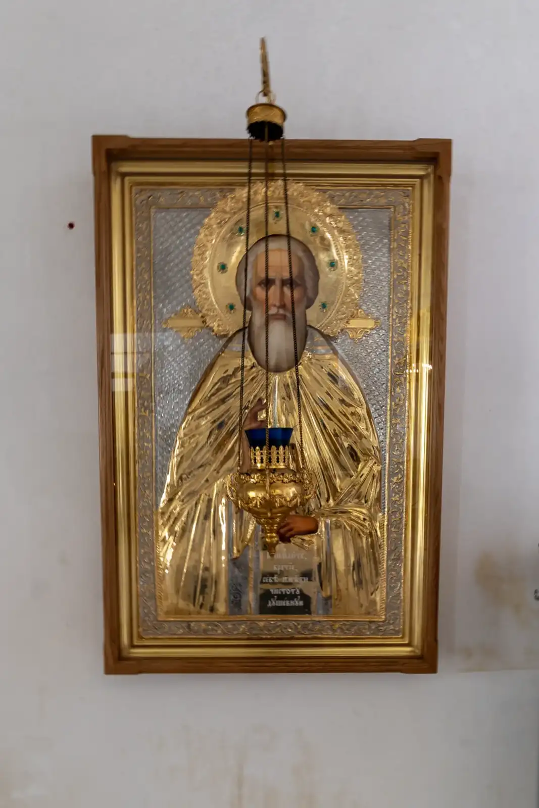 Une icône religieuse dorée et argentée représentant un saint chrétien sur un mur blanc.