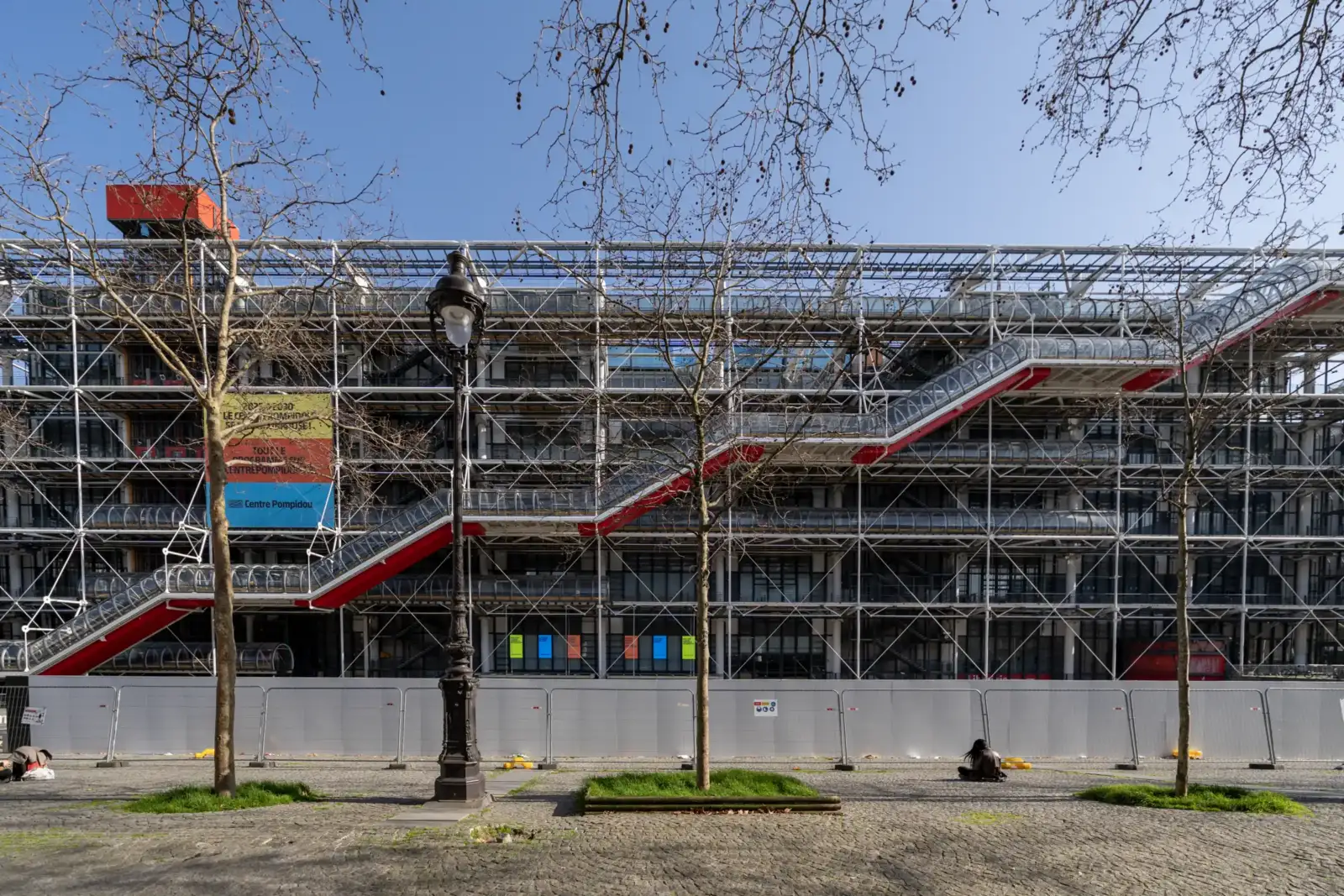 La façade industrielle du Centre Pompidou se dresse derrière des arbres sur une place.