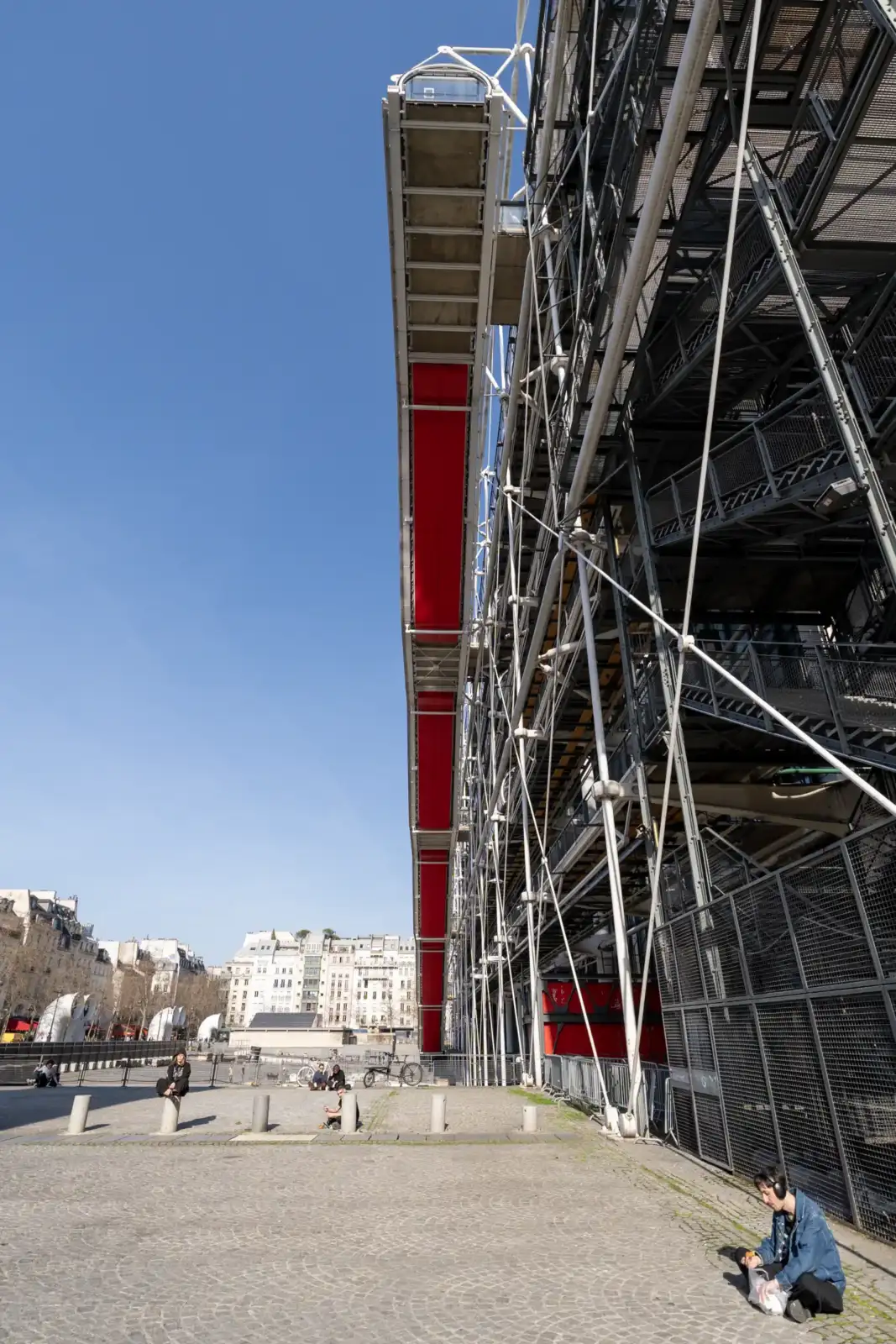 La façade industrielle du Centre Pompidou avec son escalier rouge sous un ciel bleu.