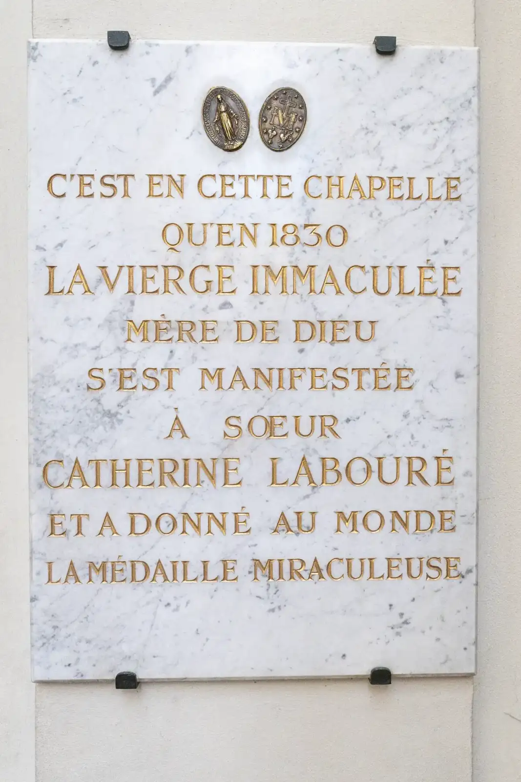 Plaque en marbre blanc avec des lettres dorées commémorant les apparitions mariales de 1830.