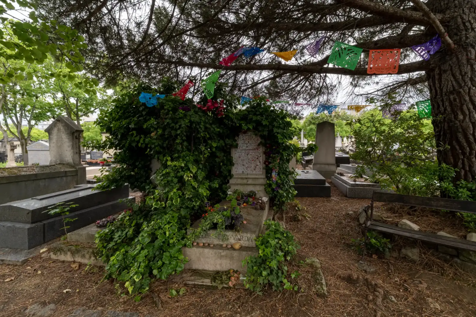 Une tombe recouverte de lierre est décorée de guirlandes colorées dans un cimetière parisien.