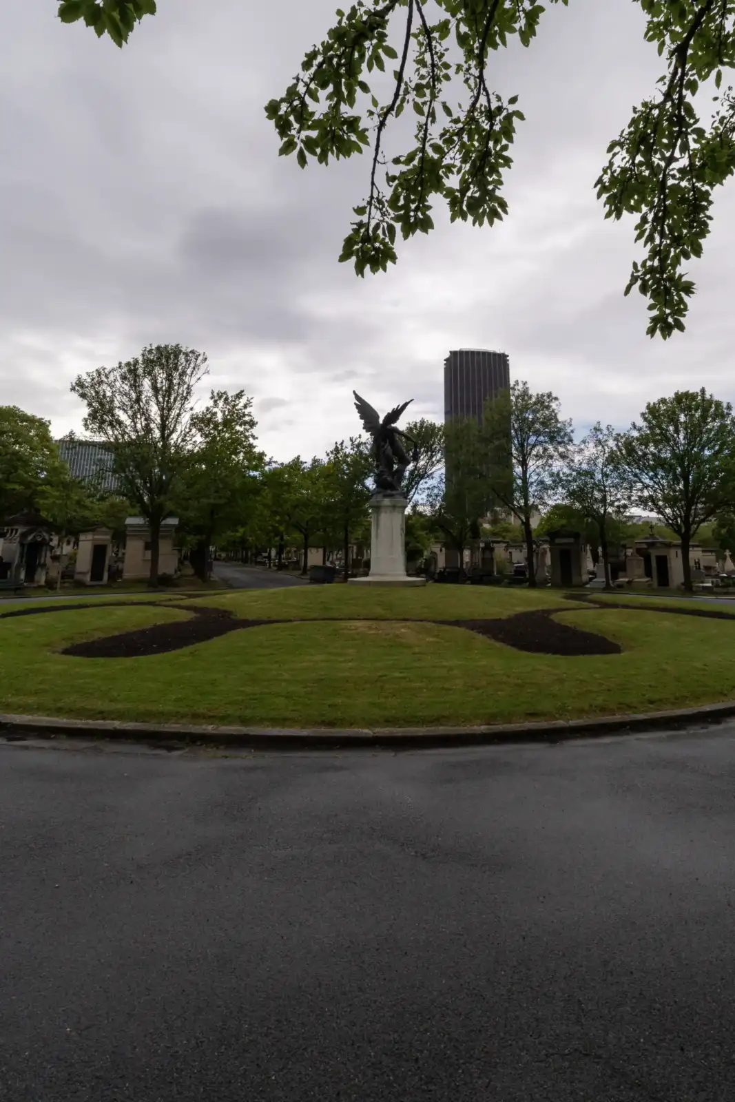 Une statue d ange sur un rond-point arboré surplombe les allées du cimetière parisien.