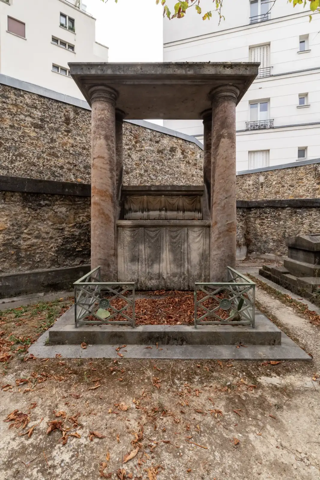 Un monument funéraire antique à colonnes entouré de murs anciens et d immeubles parisiens.