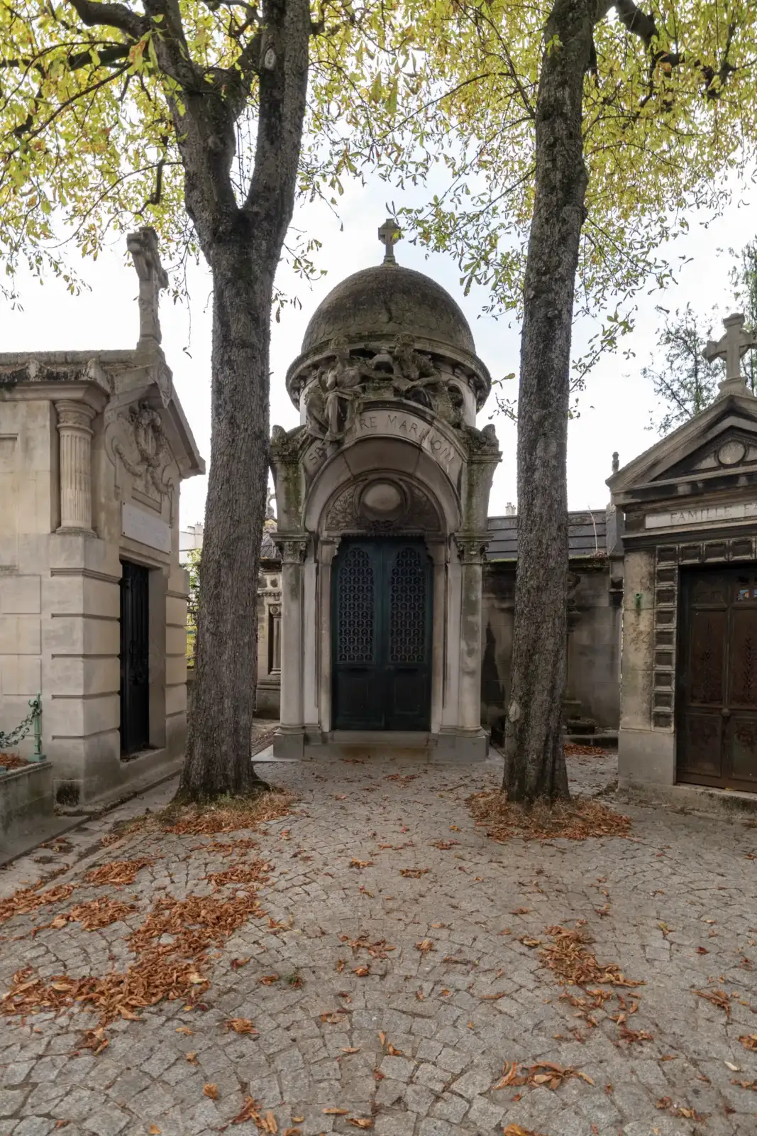 Façade d'un monument funéraire à dôme dans un cimetière parisien encadré par des arbres.