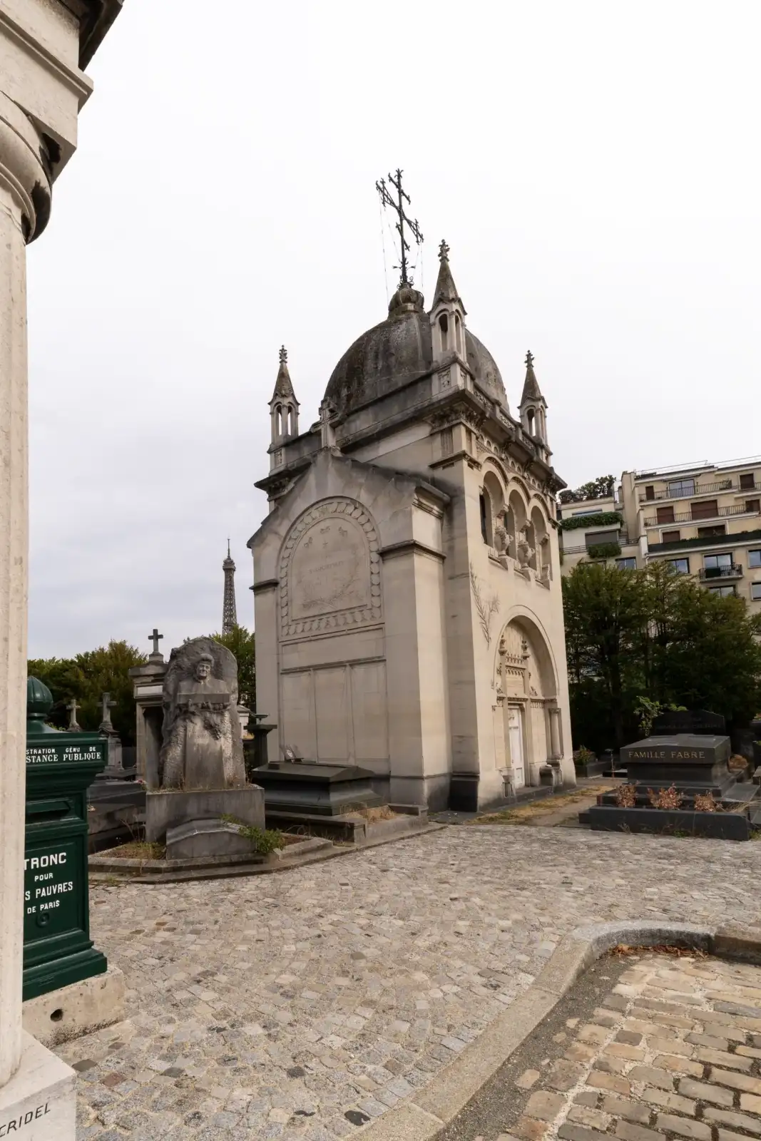 La façade d un grand mausolée de pierre du cimetière de Passy avec la Tour Eiffel au fond.