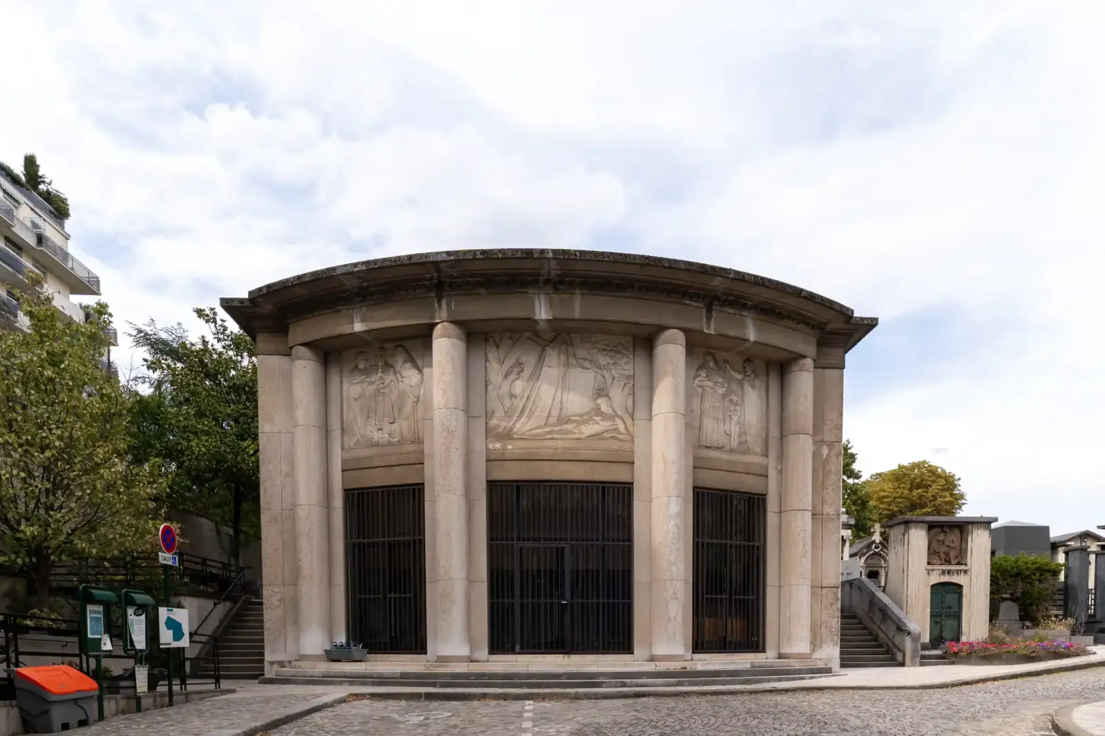 Façade en demi-cercle d'un monument funéraire parisien orné de colonnes et bas-reliefs sculptés.